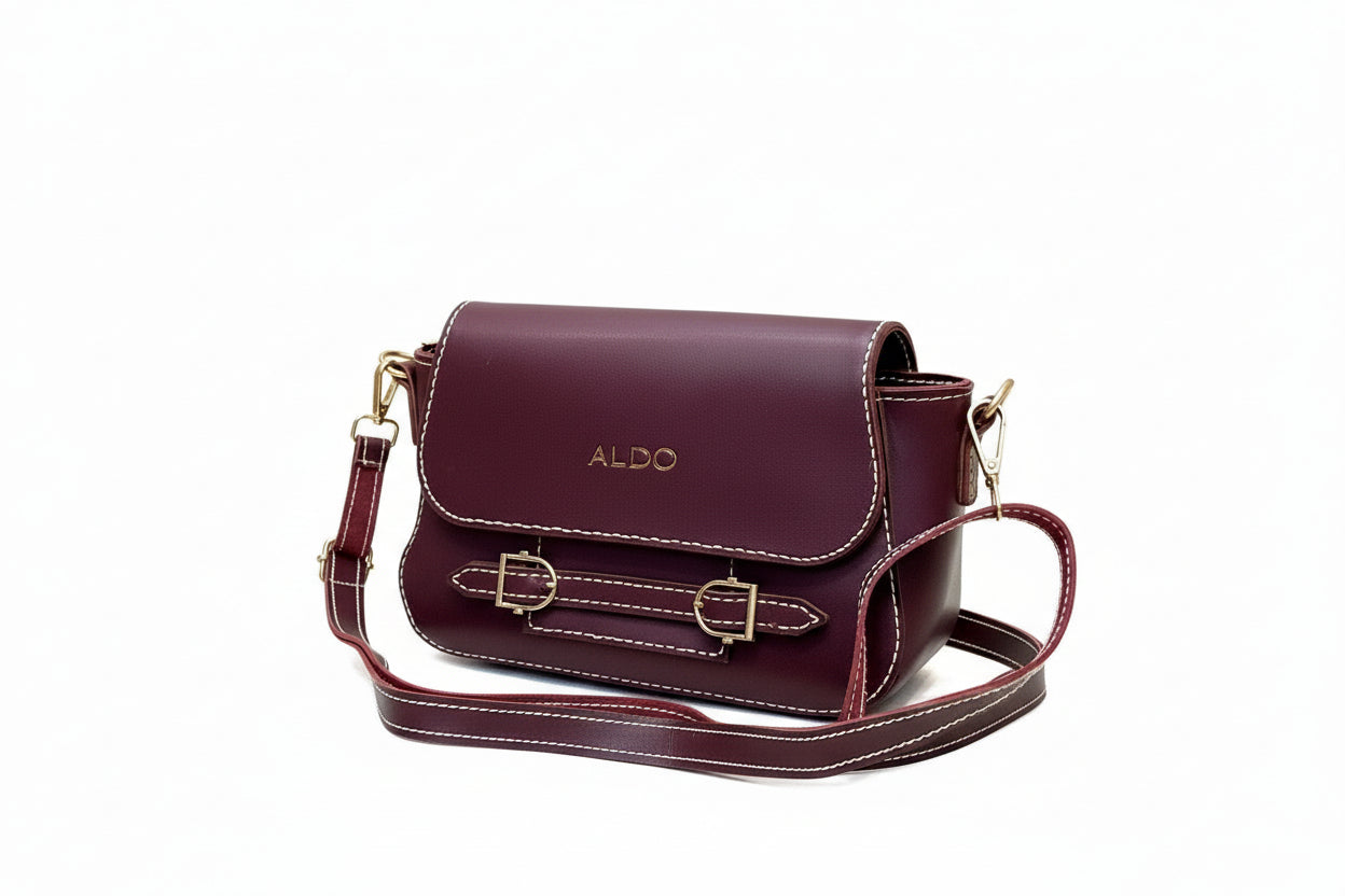 Maroon handbag with gold accents on a white surface with a wooden background