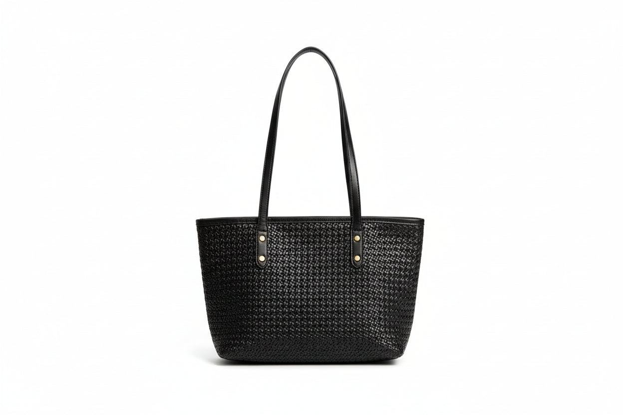 Person holding a black woven handbag with a plain background
