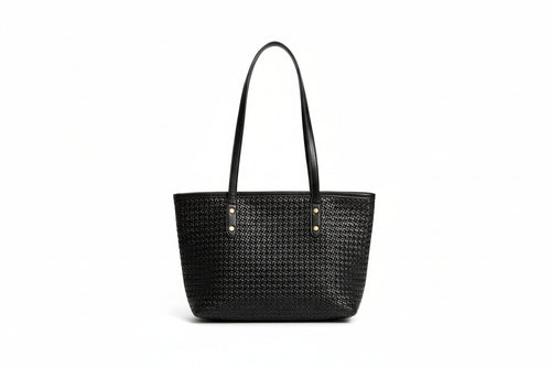 Person holding a black woven handbag with a plain background