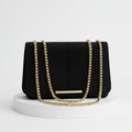 Black handbag with gold chain on a beige background