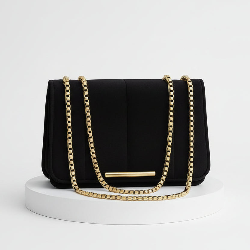 Black handbag with gold chain on a beige background